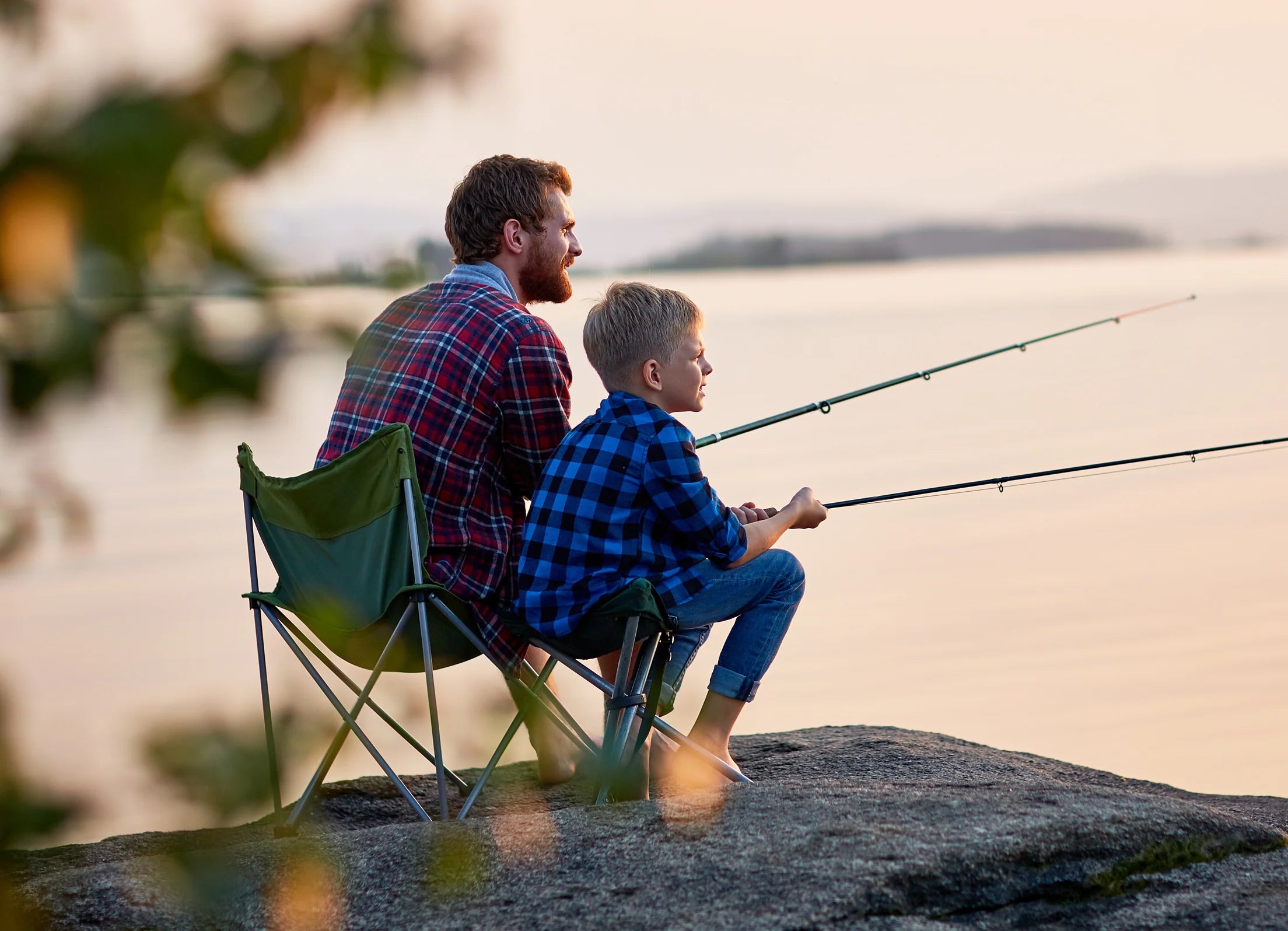 A father and son sitting on chairs at the lake, fishing together