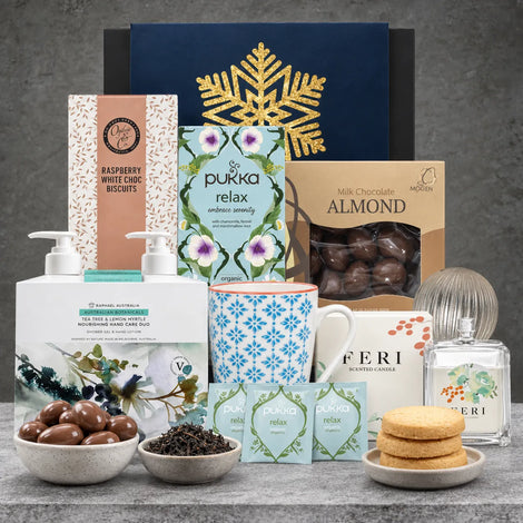 Festive Relax and Restore pamper hamper featuring a patterned mug, scented candle, tea tree hand wash and lotion, organic relax tea, chocolate almonds and raspberry white chocolate biscuits